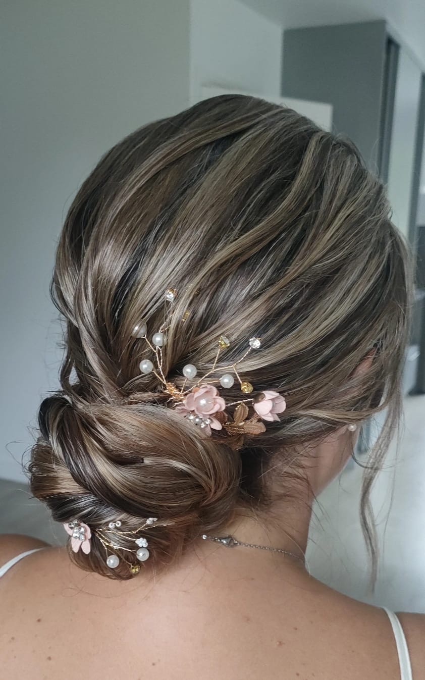 Chignon bas flou orné de fleurs rose poudré et d'épingles perlées, vu de dos
