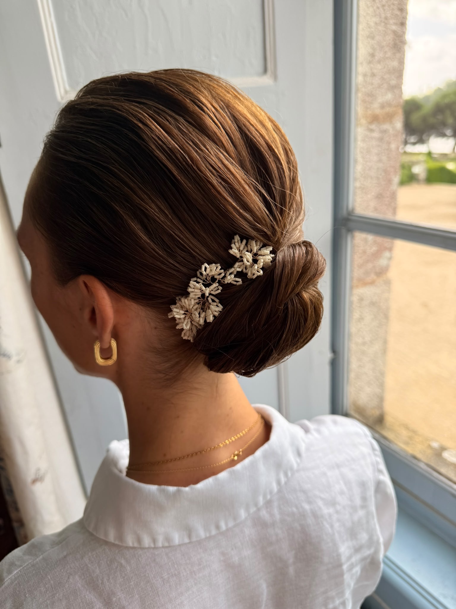 Chignon bas lisse de mariée orné d'une barrette de fleurs dorées et de perles, réalisé près de Perros-Guirec
