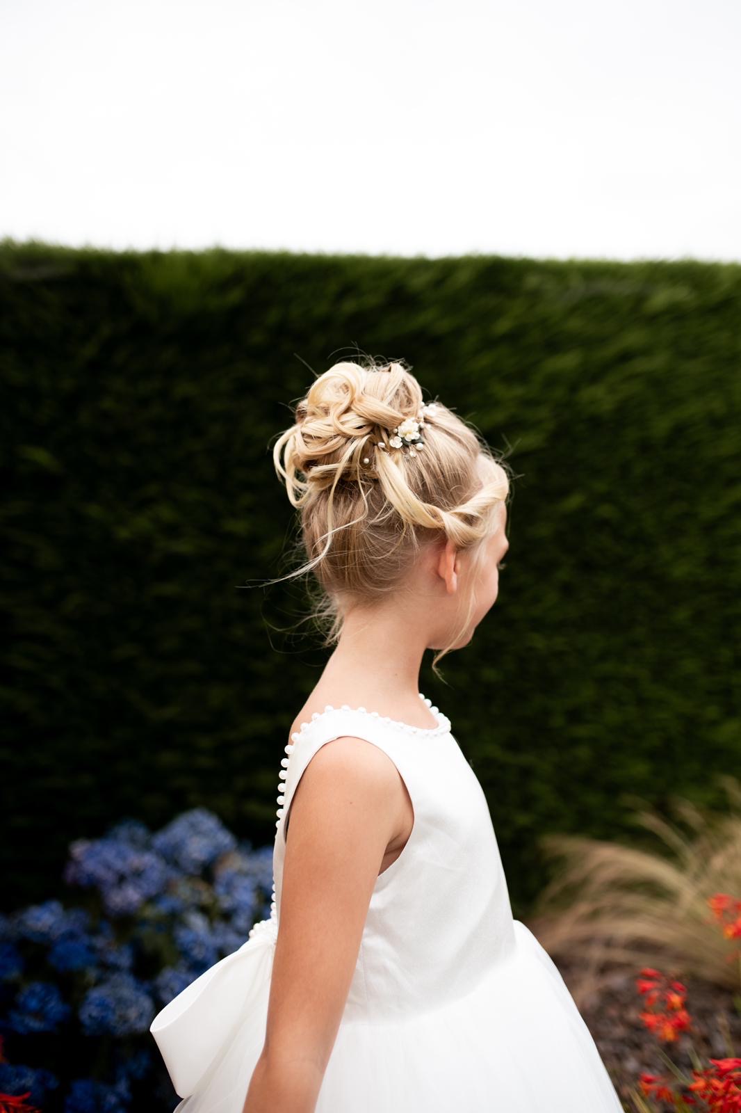 Chignon haut bouclé d'une petite fille d'honneur en robe blanche