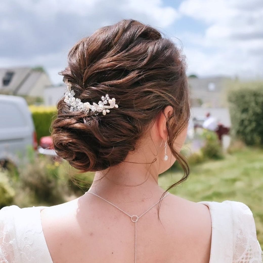 Chignon flou de mariée avec peigne fleuri, photographié en extérieur pendant le vin d'honneur